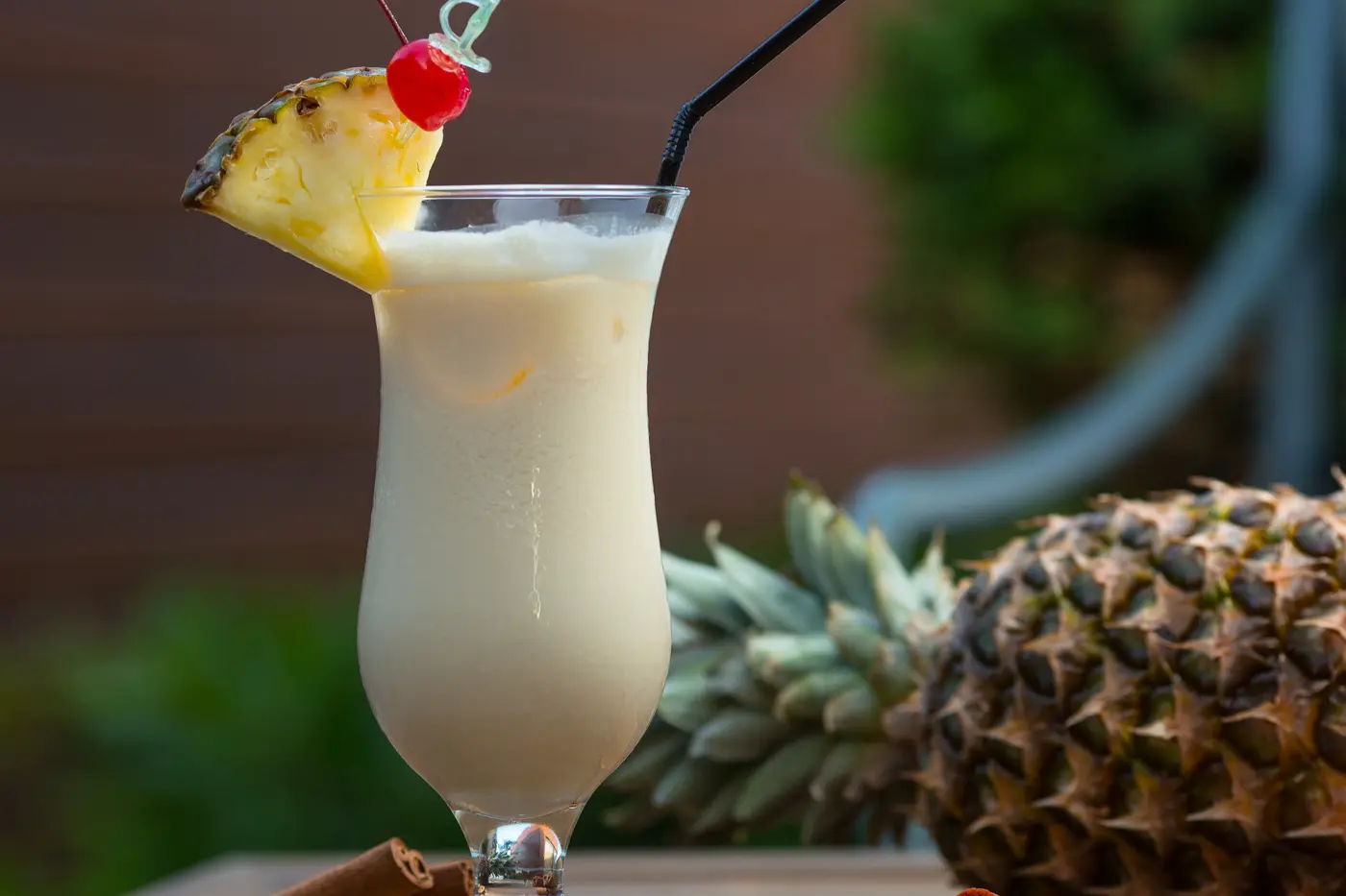 A tall pineapple drink garnished with fruit, beside a whole pineapple